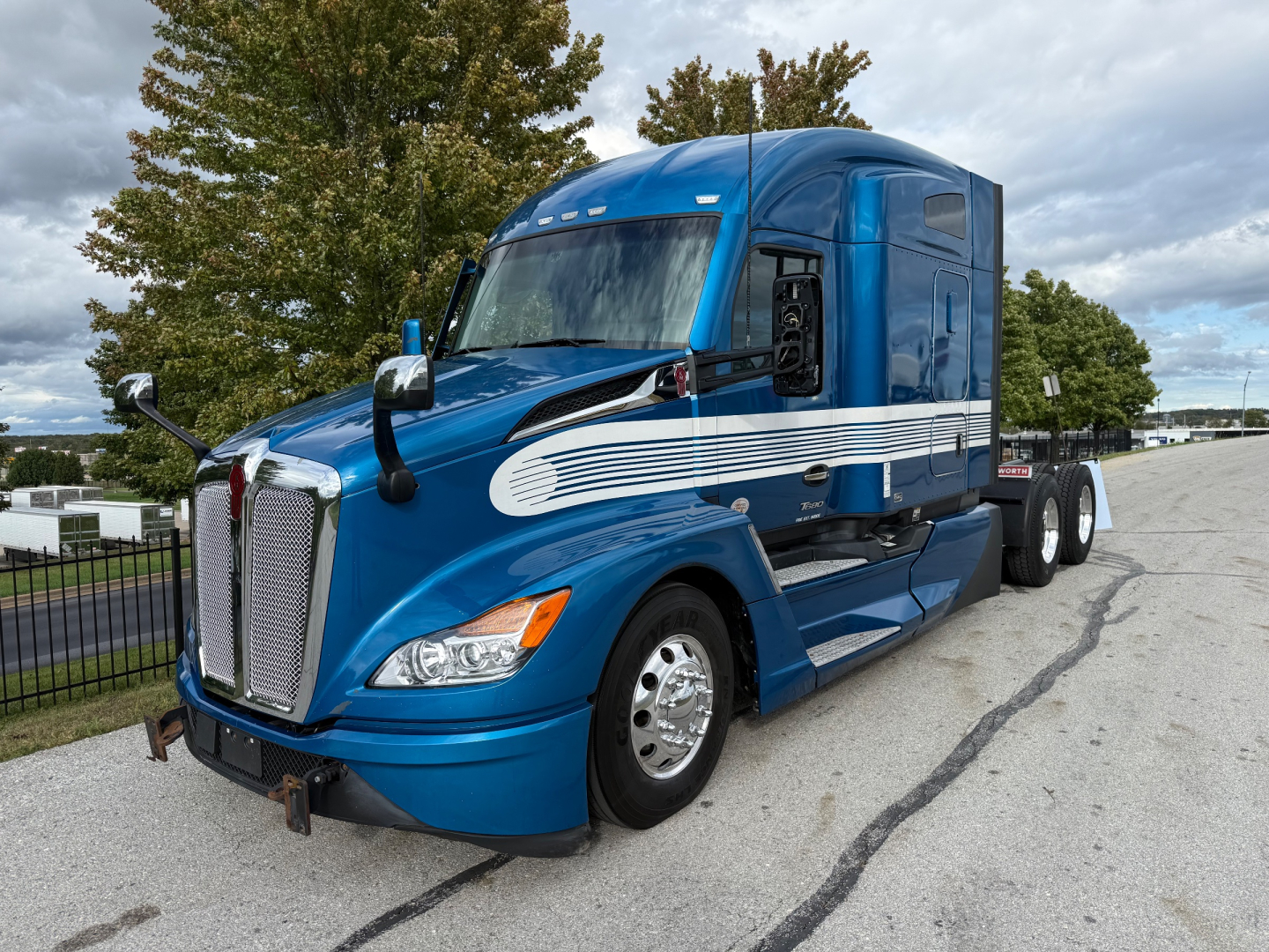 Kenworth T680 tractor in blue, front-left view, with chrome grille and side stripe decal. Cab high-rise sleeper, dual rear axles, empty fifth wheel, side mirrors, headlights visible.