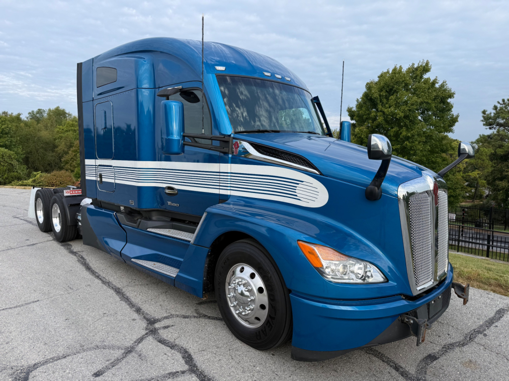 Blue 2024 Kenworth T680 sleeper cab truck shown from front-left angle with chrome grille and white stripe decals.