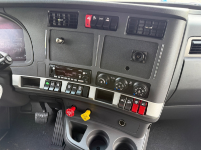 Kenworth T680 cab interior dashboard showing control switches, gauges, ignition area with yellow and red keys hanging, and storage compartments.