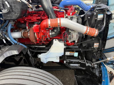 Kenworth T680 engine bay showing red engine block, gray intake tubing, blue silicone hoses, white coolant reservoir, and black radiator support.