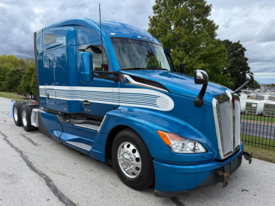 Blue Kenworth T680 tractor-trailer cab from a front-side angle showing chrome grille, headlights, and mirrors.