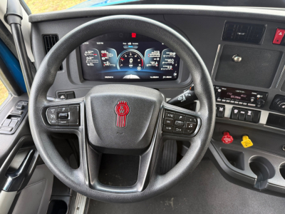 Kenworth T680 truck interior showing steering wheel with red emblem, digital dashboard, center console with controls, and cup holders.