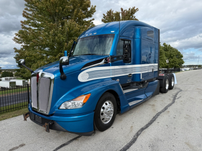Kenworth T680 tractor in blue, front-left view, with chrome grille and side stripe decal. Cab high-rise sleeper, dual rear axles, empty fifth wheel, side mirrors, headlights visible.