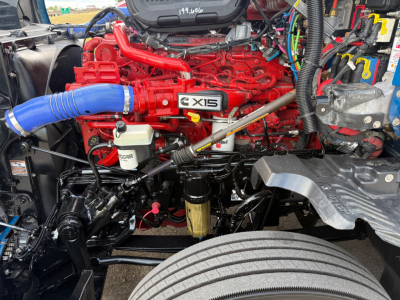 Kenworth T680 engine bay with red engine block, X15 badge, blue intercooler hose, white coolant reservoir, and various black hoses and wiring in view.