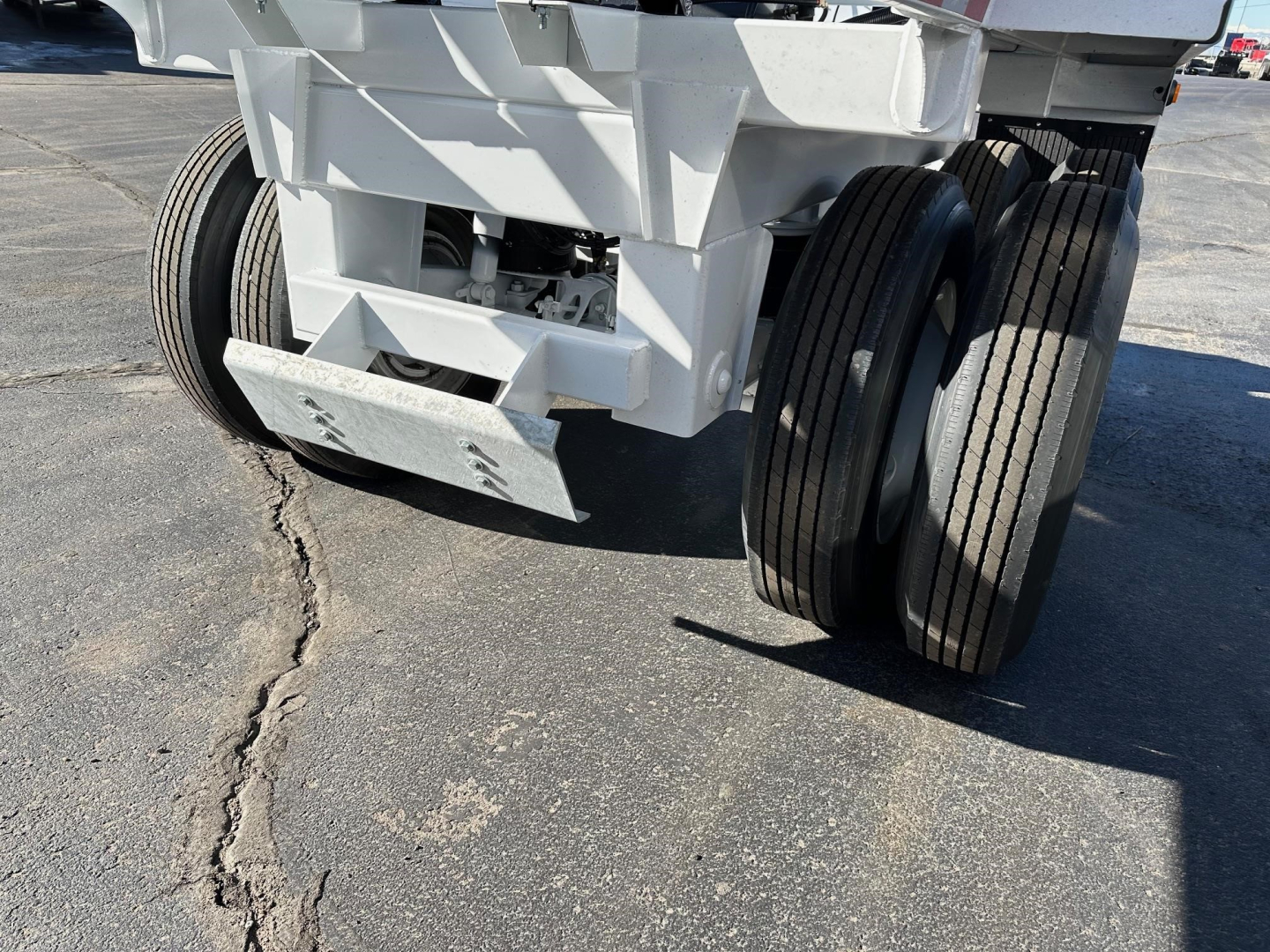 Dump trailer bottom view showing dual rear axles and white cargo bed structure with wheels.