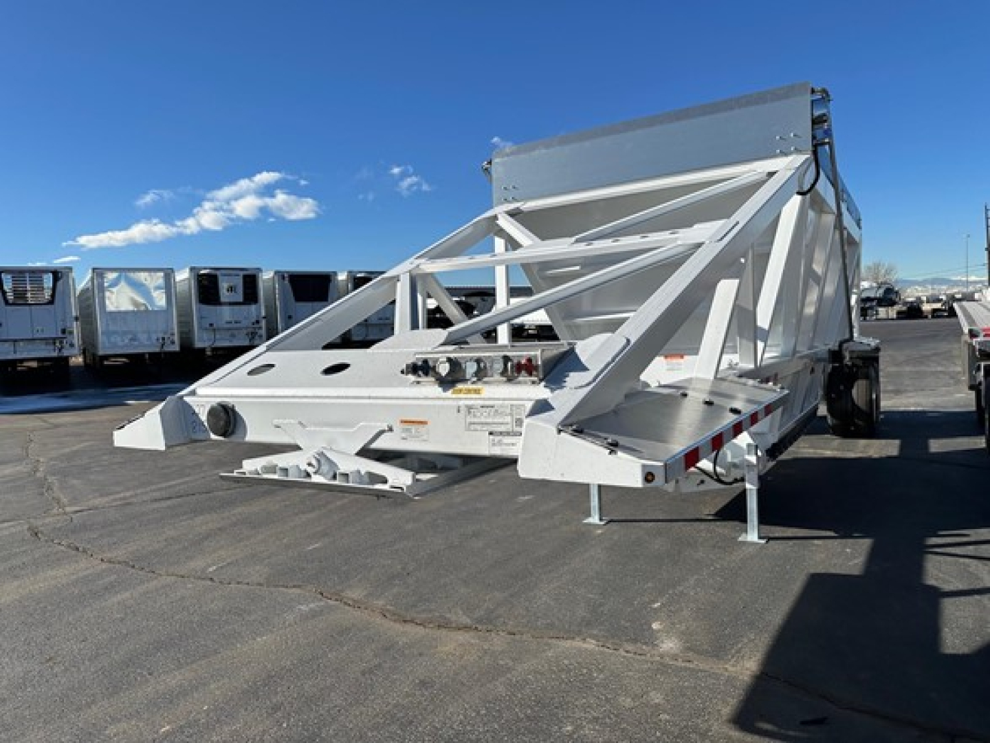 CPS Air Ride Bottom Dump trailer in front of a row of white trailers, white frame structure, raised dumping body, on a paved lot.