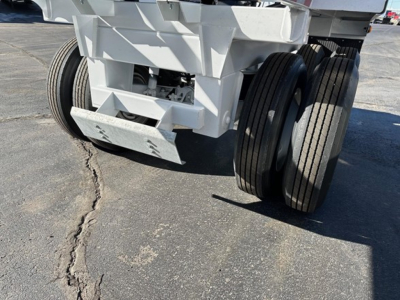 Dump trailer rear view showing dual rear axles and heavy-duty white steel frame with hydraulic bottom dump mechanism.