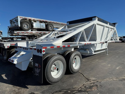 CPS air ride bottom dump trailer viewed from rear-left showing dual-axle configuration, white frame with triangular truss, and a spare trailer on a flatbed behind.