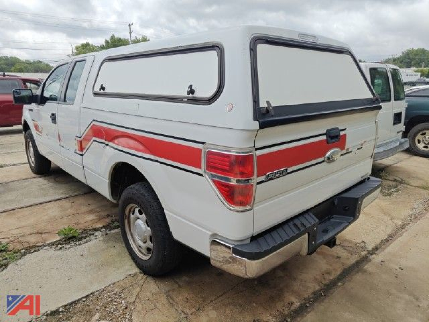 Ford F-150 pickup with cap, rear view showing toolbox-cap cover and emergency truck styling decal along side, white with red stripe.