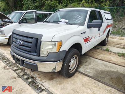 Ford F-150 crew cab emergency truck with cap, front-left view, gray body with black grille and bumper, emergency decals along side.