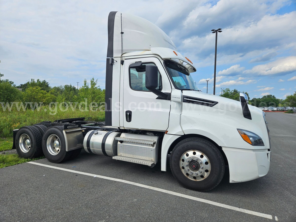 Freightliner Cascadia tractor trailer in a parking lot showing side profile, cab with sleeper, and dual rear axles.