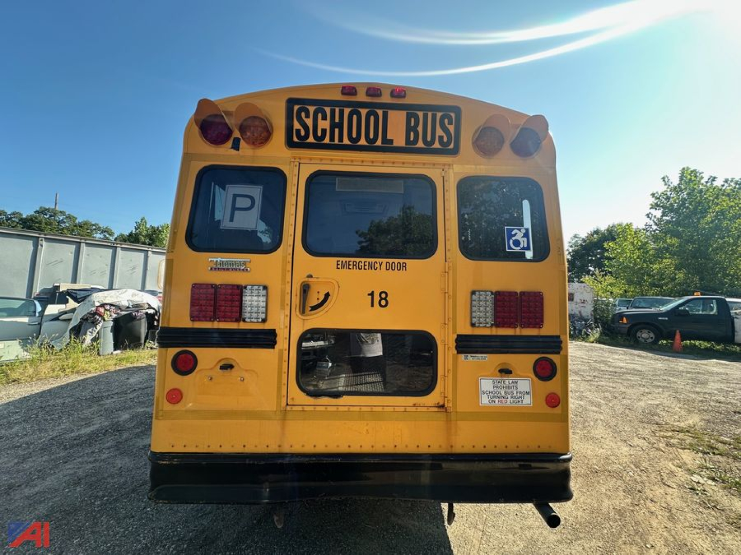 Rear view of a yellow school bus labeled SCHOOL BUS with wheelchair accessibility graphics and emergency door, 18 number, parked in a lot.
