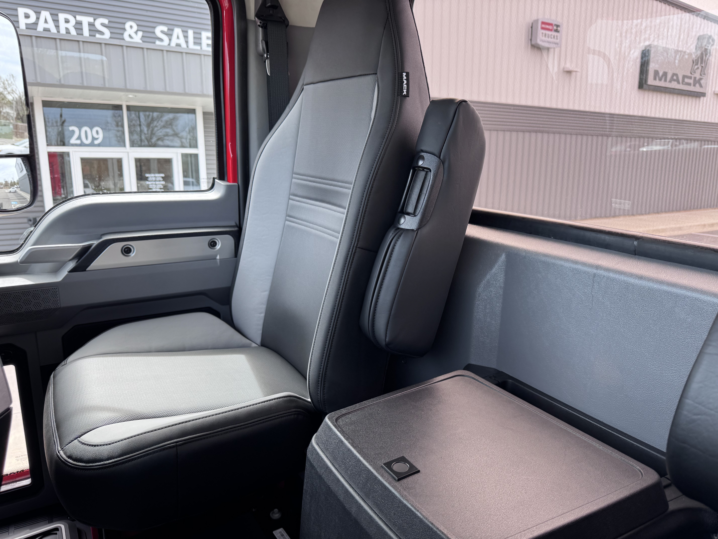 Cab interior of a 2027 Mack PI64T truck showing captain seat, passenger seat, and center console/storage box.