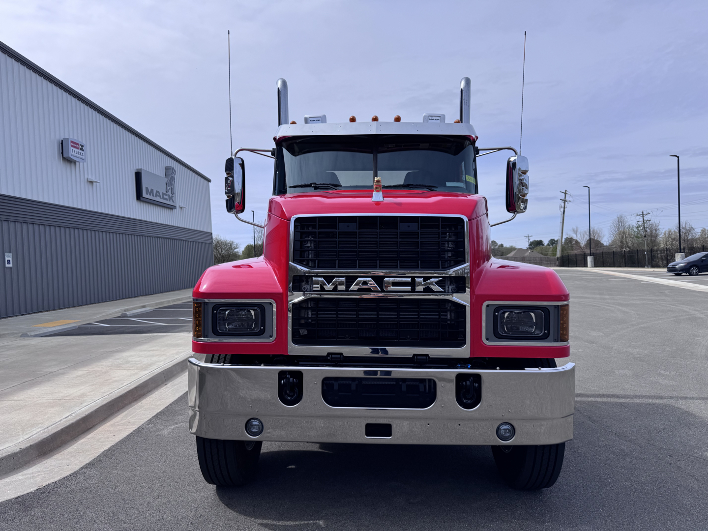 Front view of a red 2027 Mack PI64T conventional daycab truck with large black grille, chrome bumper, and dual vertical exhaust stacks.