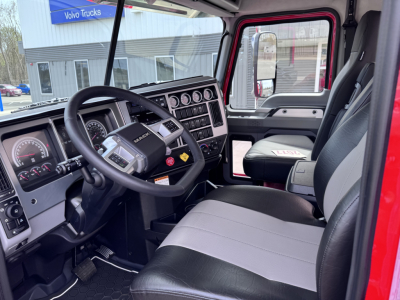 Dashboard and driver’s seat of a 2027 Mack PI64T daycab showing steering wheel, gauges, and console.