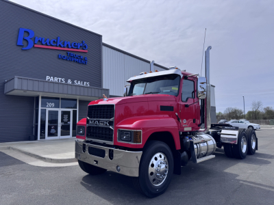 Mack PI64T conventional daycab truck front-left view in dealership lot with chrome bumper, dual rear axles, red cab, and Bruckner's Trucks sign in background.