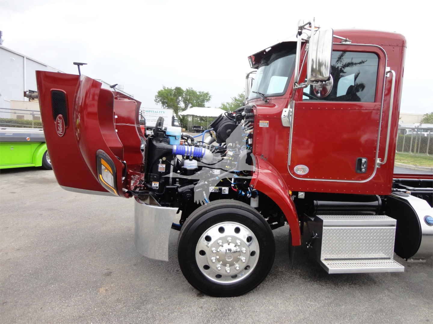 2022 Peterbilt 337 rollback truck with hood raised, showing engine components and chrome exhaust, red cab, front wheel and chrome fuel steps.