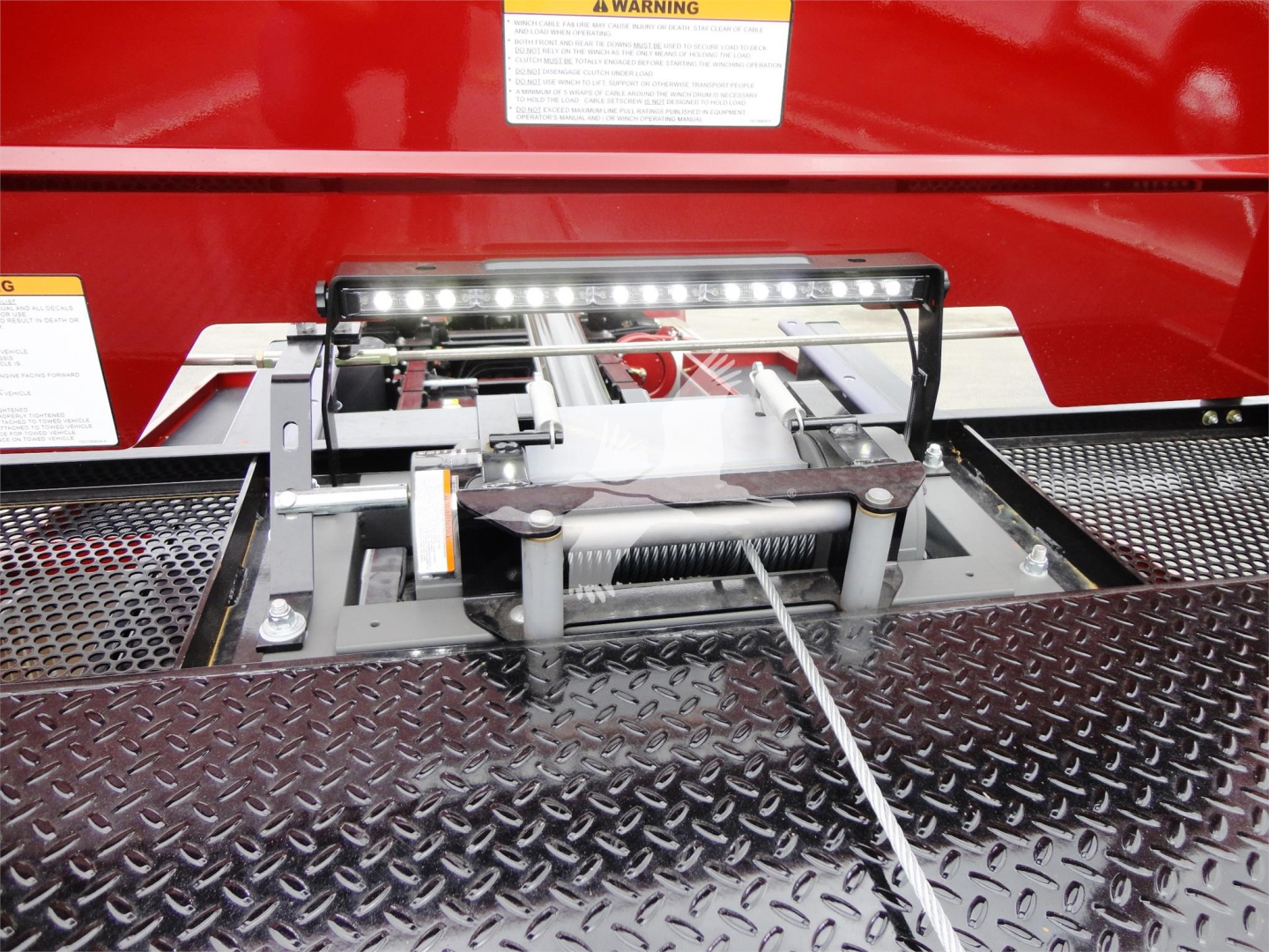 Peterbilt 337 rollback truck hitch mechanism mounted on diamond plate platform with LED light bar above, red body in background