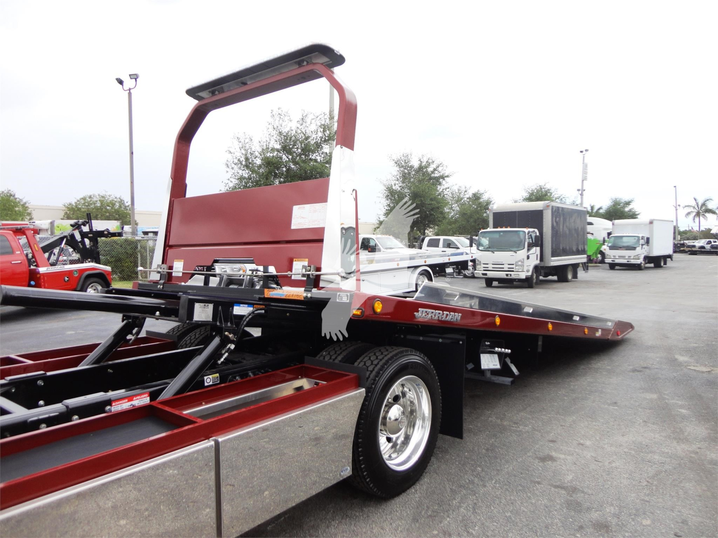 Peterbilt 337 rollback tow truck with a red/tower apparatus and flatbed, showing a white 'H' style wheel fender and chrome toolbox. Visible text includes 'J06173 FM' and 'ROLLBACK' on the side; other vehicles in background.