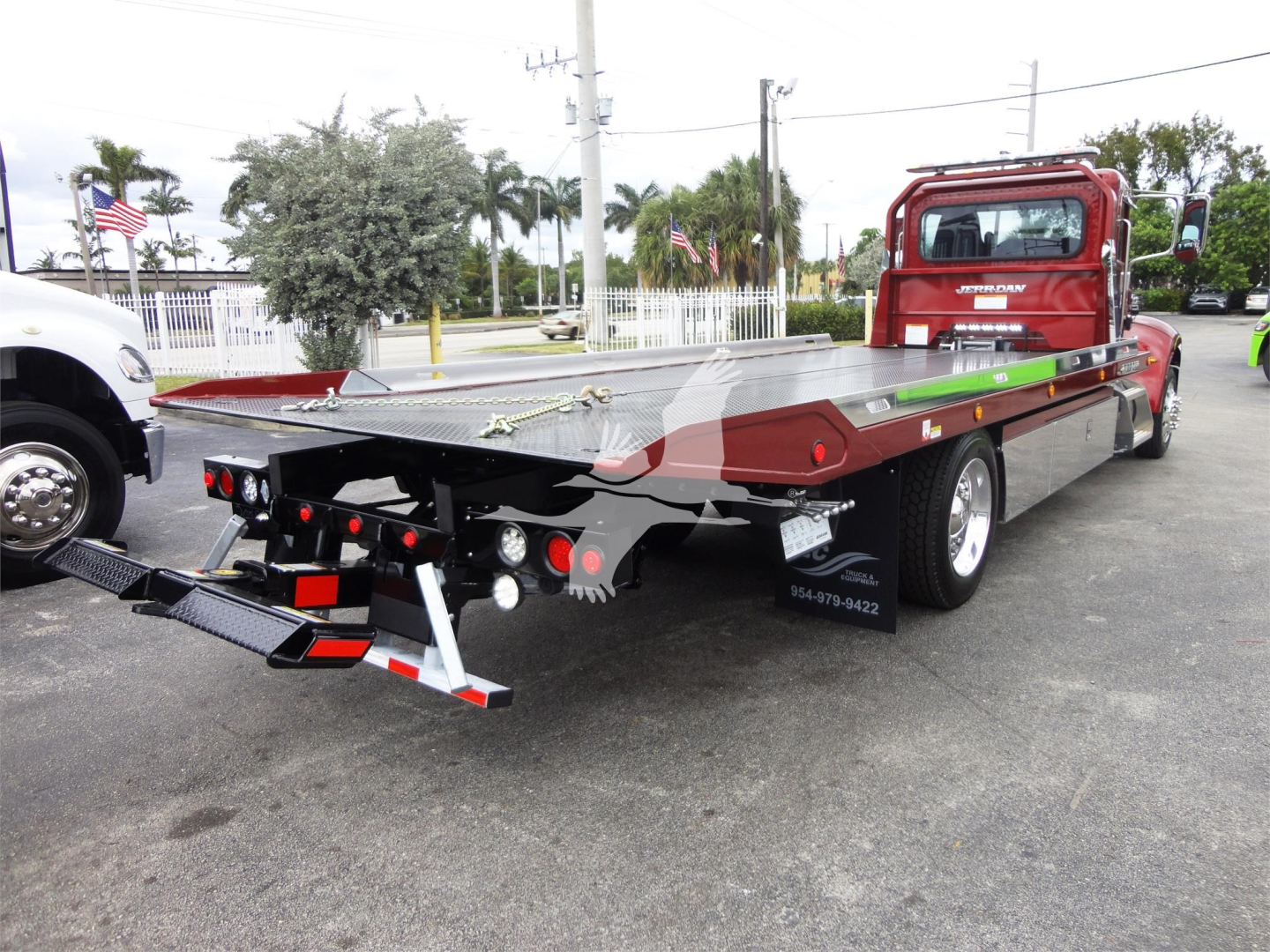 Peterbilt 337 rollback truck seen from rear-left angle with a flatbed and loading ramps, red cab, long aluminum bed, tail lights and reflectors visible.