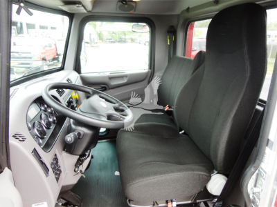 Truck cabin interior of a 2022 Peterbilt 337 rollback showing steering wheel, dash gauges, and front bench seat.
