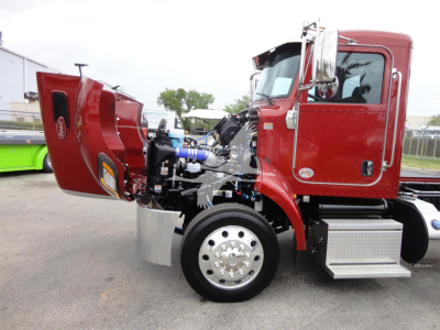 2022 Peterbilt 337 rollback truck with hood raised, showing engine components and chrome exhaust, red cab, front wheel and chrome fuel steps.