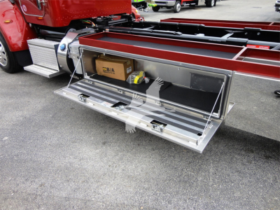 Peterbilt 337 rollback truck with open rear storage compartment showing chrome toolbox area and a cardboard SBIA box inside.