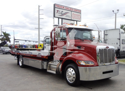 Peterbilt 337 rollback tow truck in red with chrome front and flatbed, parked at a dealership lot