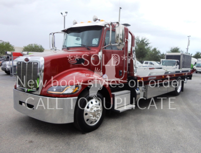 Peterbilt 337 rollback truck in red with chrome front grille and flatbed, parked outdoor.