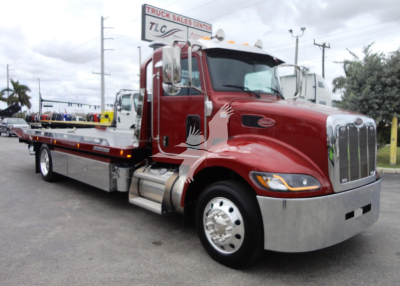 Peterbilt 337 rollback truck in red with chrome front bumper and flatbed, side view, dealership lot in background, TLC sign above.