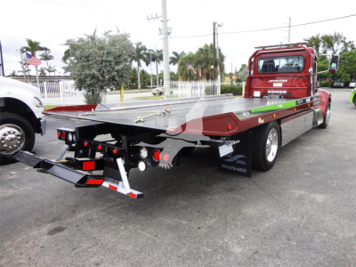 Peterbilt 337 rollback truck seen from rear-left angle with a flatbed and loading ramps, red cab, long aluminum bed, tail lights and reflectors visible.