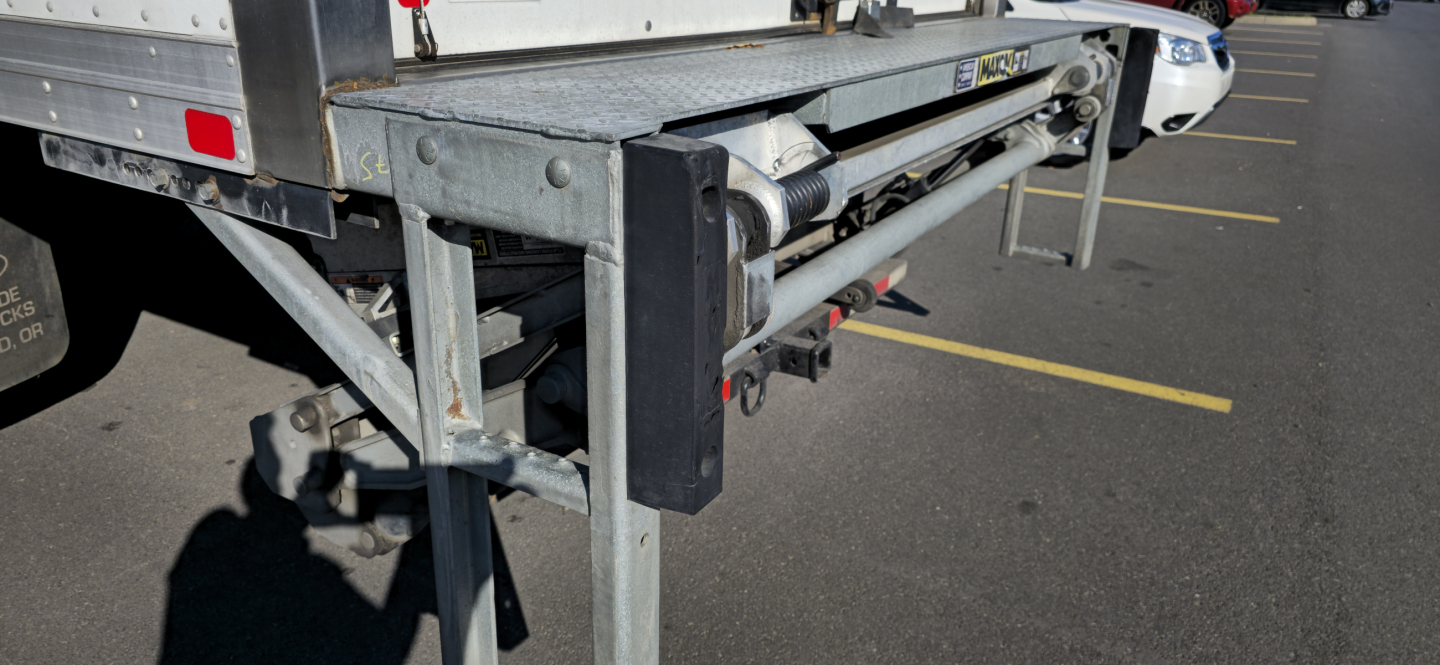 Truck bed side view showing hydraulic lift mechanism and trailer hitch on a used 2019 Ford 650 box truck.