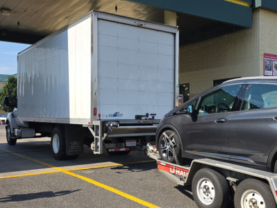 Fordbox truck in a parking lot with a white box cargo trailer and a gray SUV on a tow dolly; visible text includes 'SUMMIT' on the trailer and a license plate area at rear.
