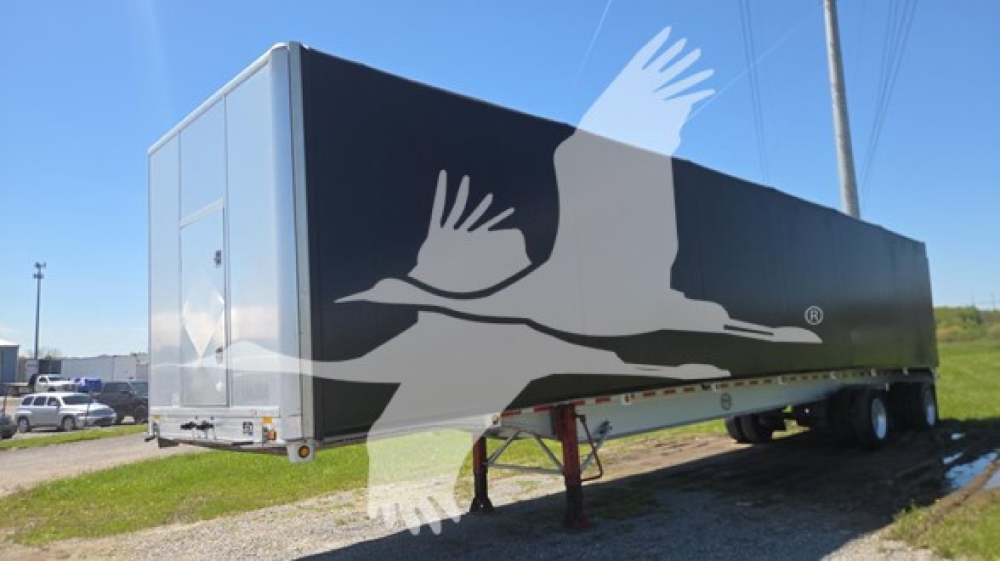 Mac aluminum flatbed trailer showing a large graphic with white birds on a black side panel and a rear door on the left.