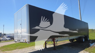 Mac aluminum flatbed trailer showing a large graphic with white birds on a black side panel and a rear door on the left.