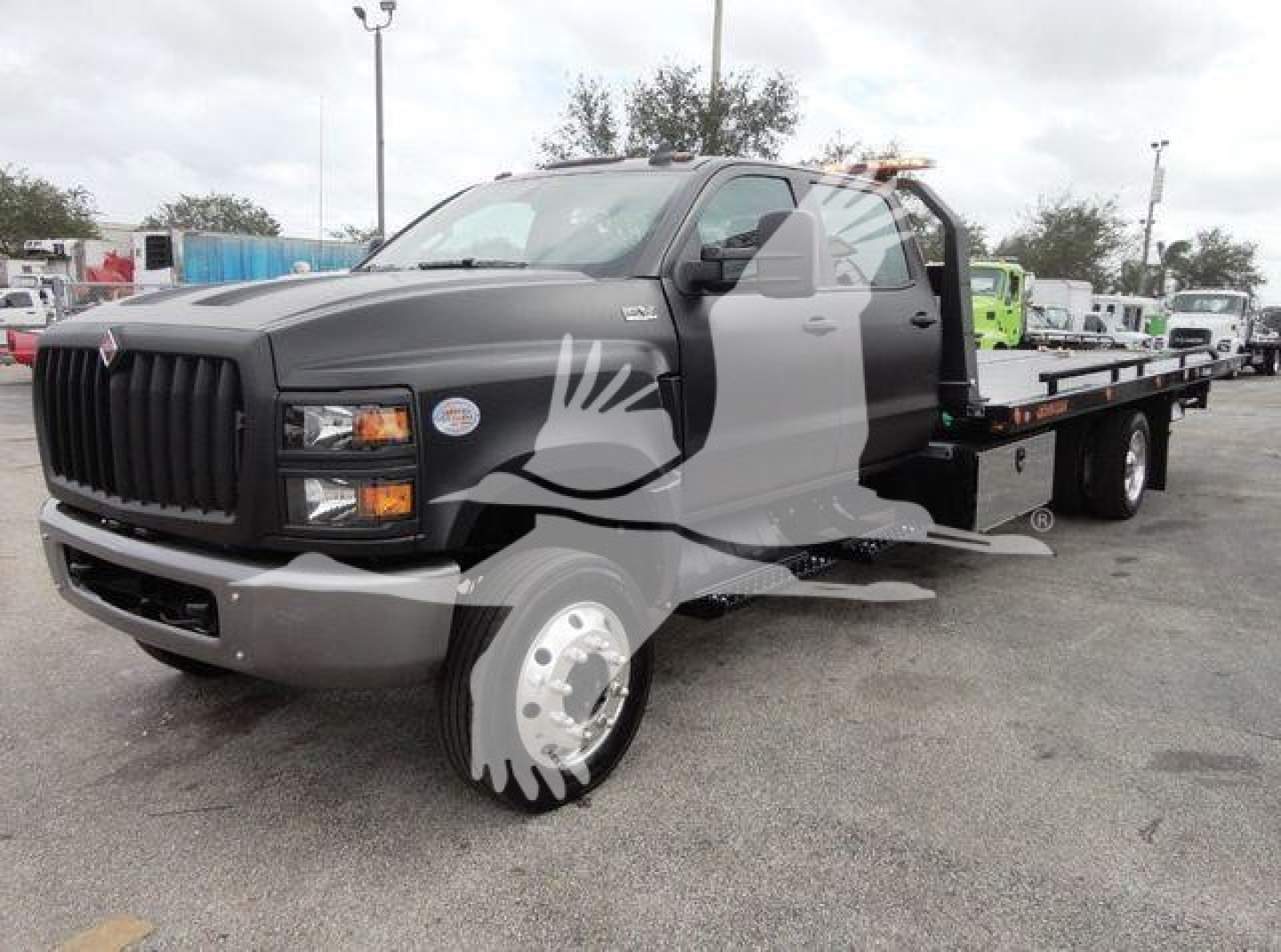 Flatbed tow truck with black cab and long steel bed, International badge on grille, watermark across image.