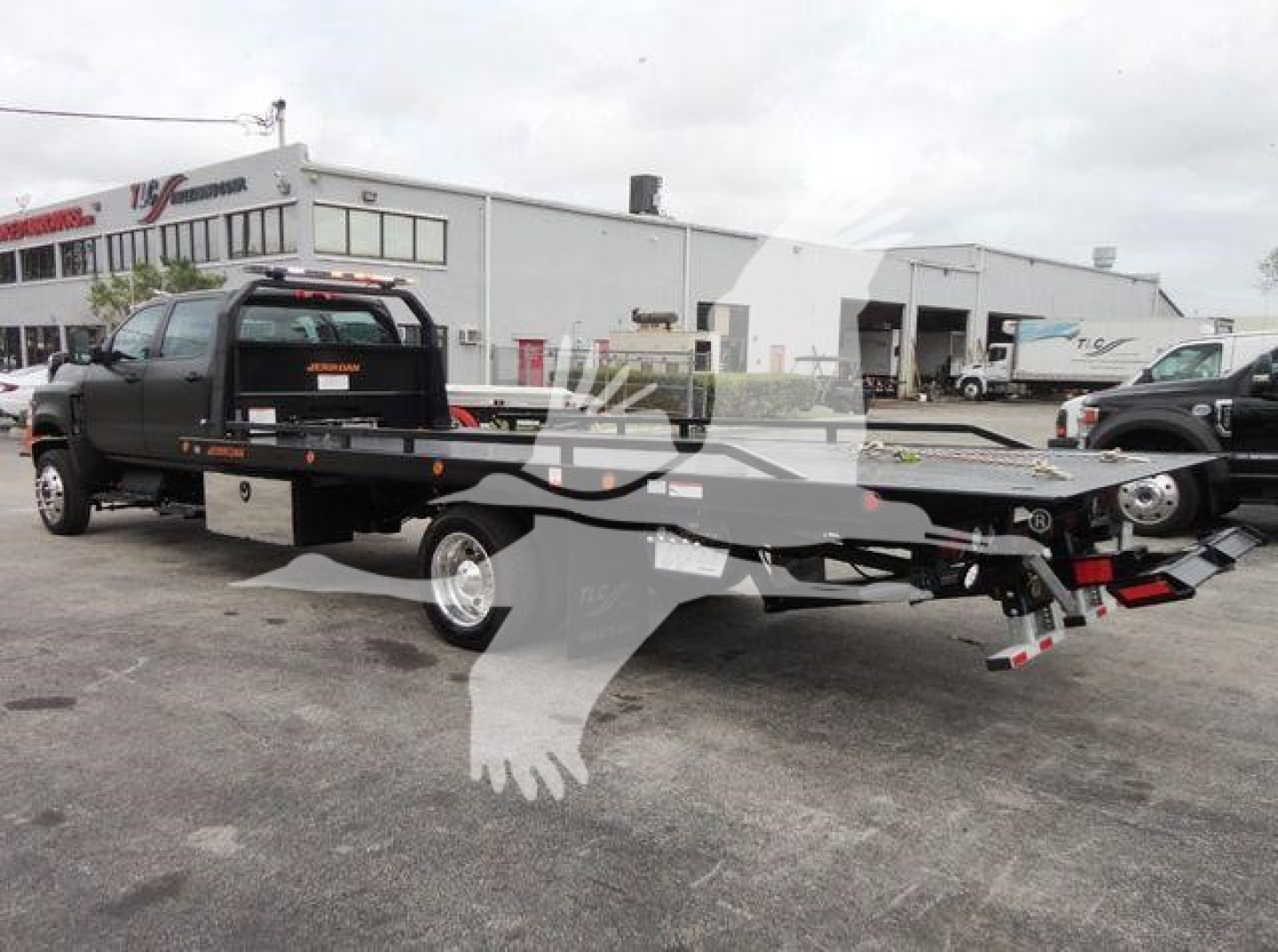 Tow truck with flatbed rollback in parking lot, black pickup front, stock number J98978, showing long flatbed and rear winch.