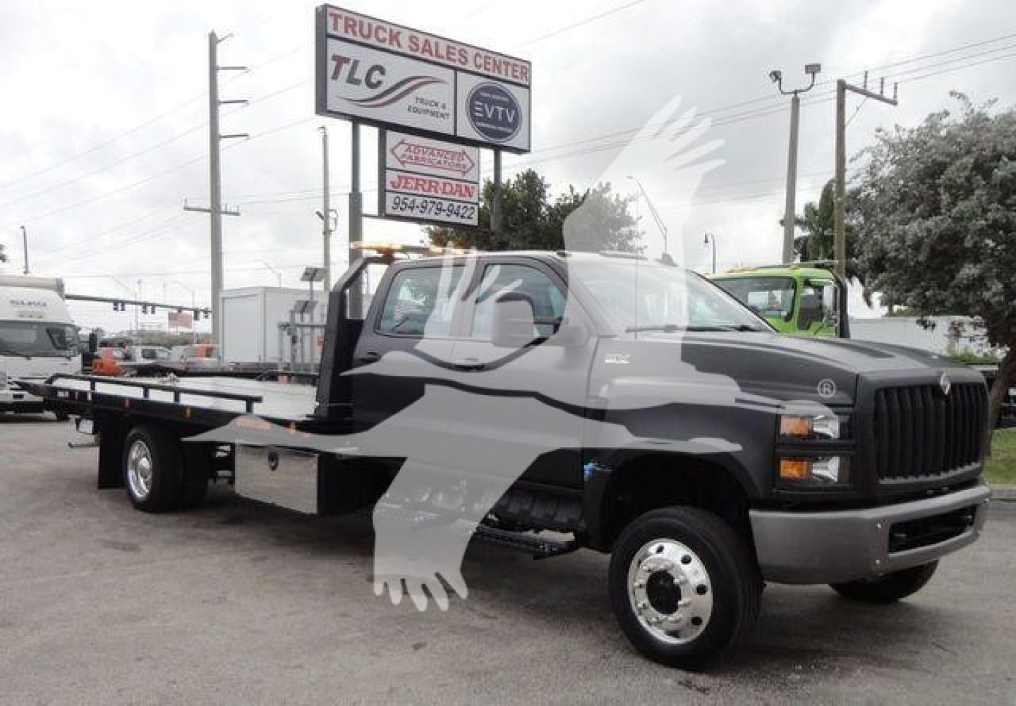2023 International CV rollback tow truck in a dealership lot showing a flatbed with dual rear wheels, cab with black grille and headlights, and signage in the background.