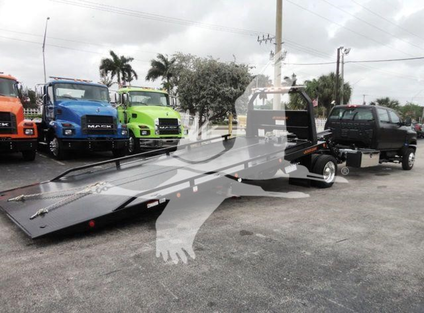 Truck rollover/flatbed trailer with black heavy-duty tow truck in background and other colorful trucks lined up; no visible model text or specs readable on image.
