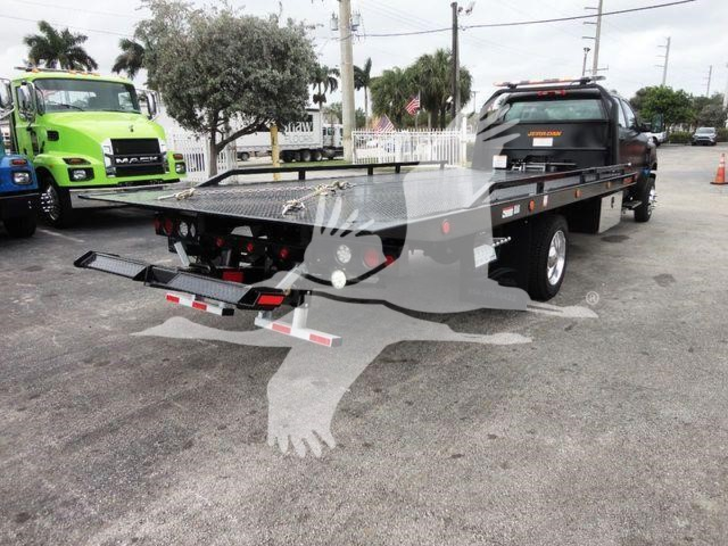Flatbed rollback tow truck trailer with rear ramps and platform, International CV equipment, seen in lot with other trucks.