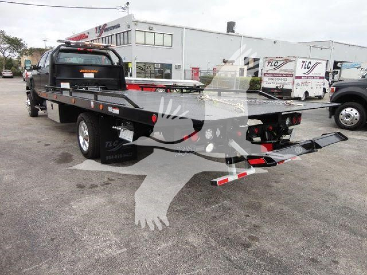 Truck flatbed wrecker equipment showing extended dovetail and ramps on a rollback truck. Side decals visible with text on the cab and rear lighting assemblies.