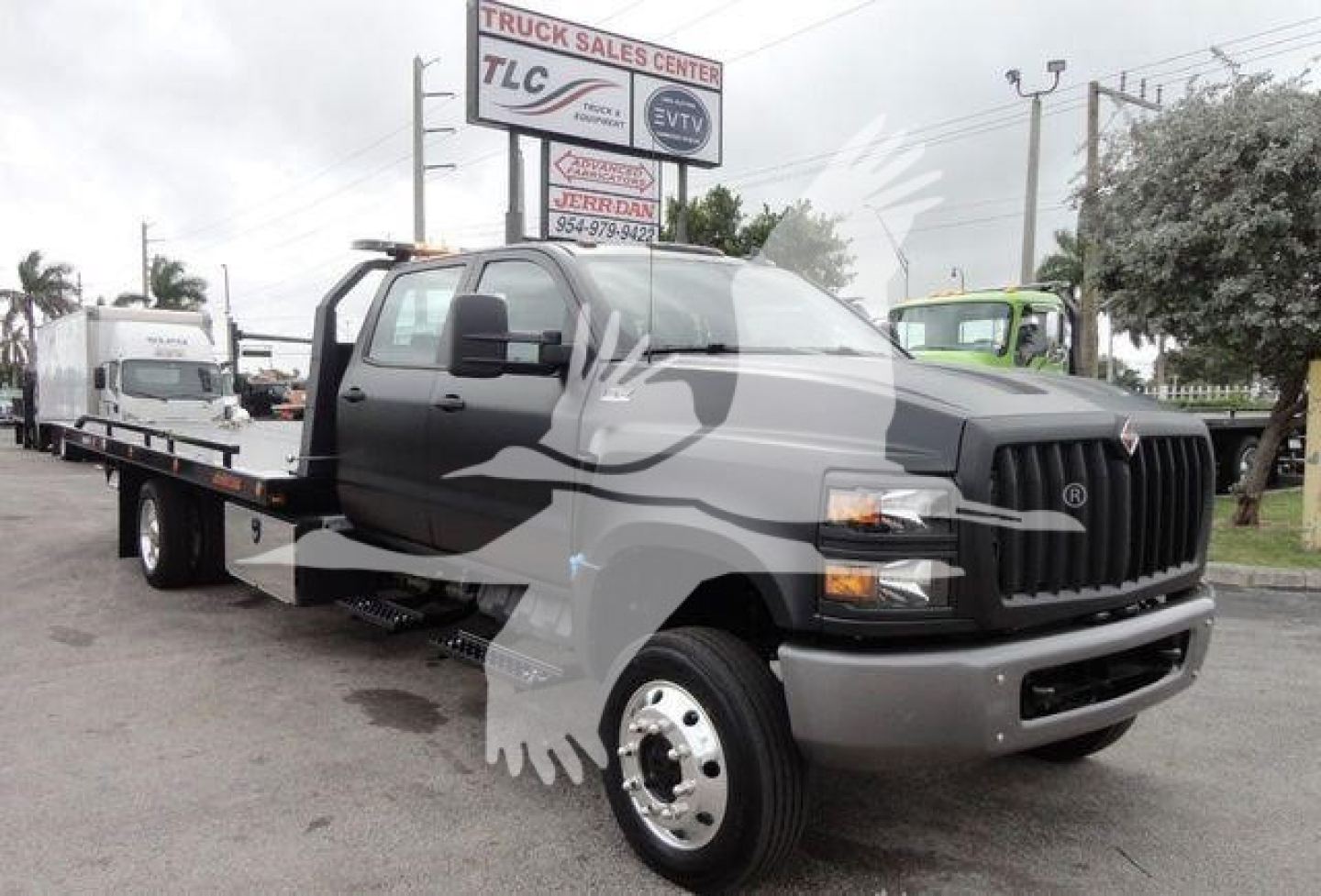 Flatbed tow truck in a dealership lot with International cab and black-gray color scheme.