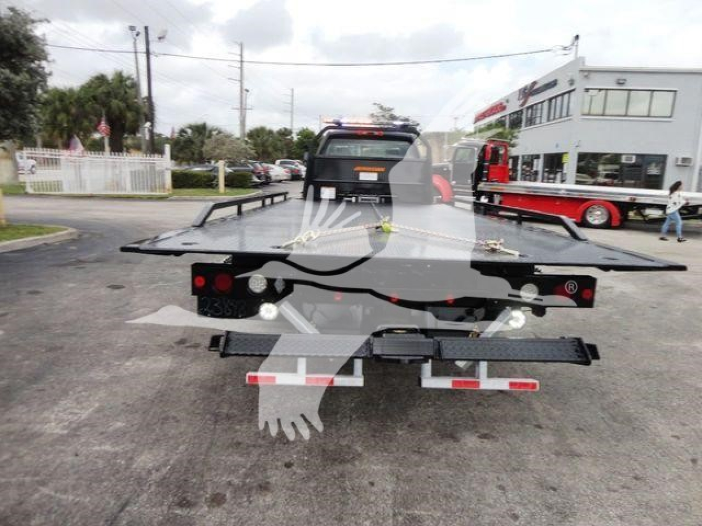 Tractor-trailer tow truck with a flatbed in a dealership lot; back view showing platform and taillights.