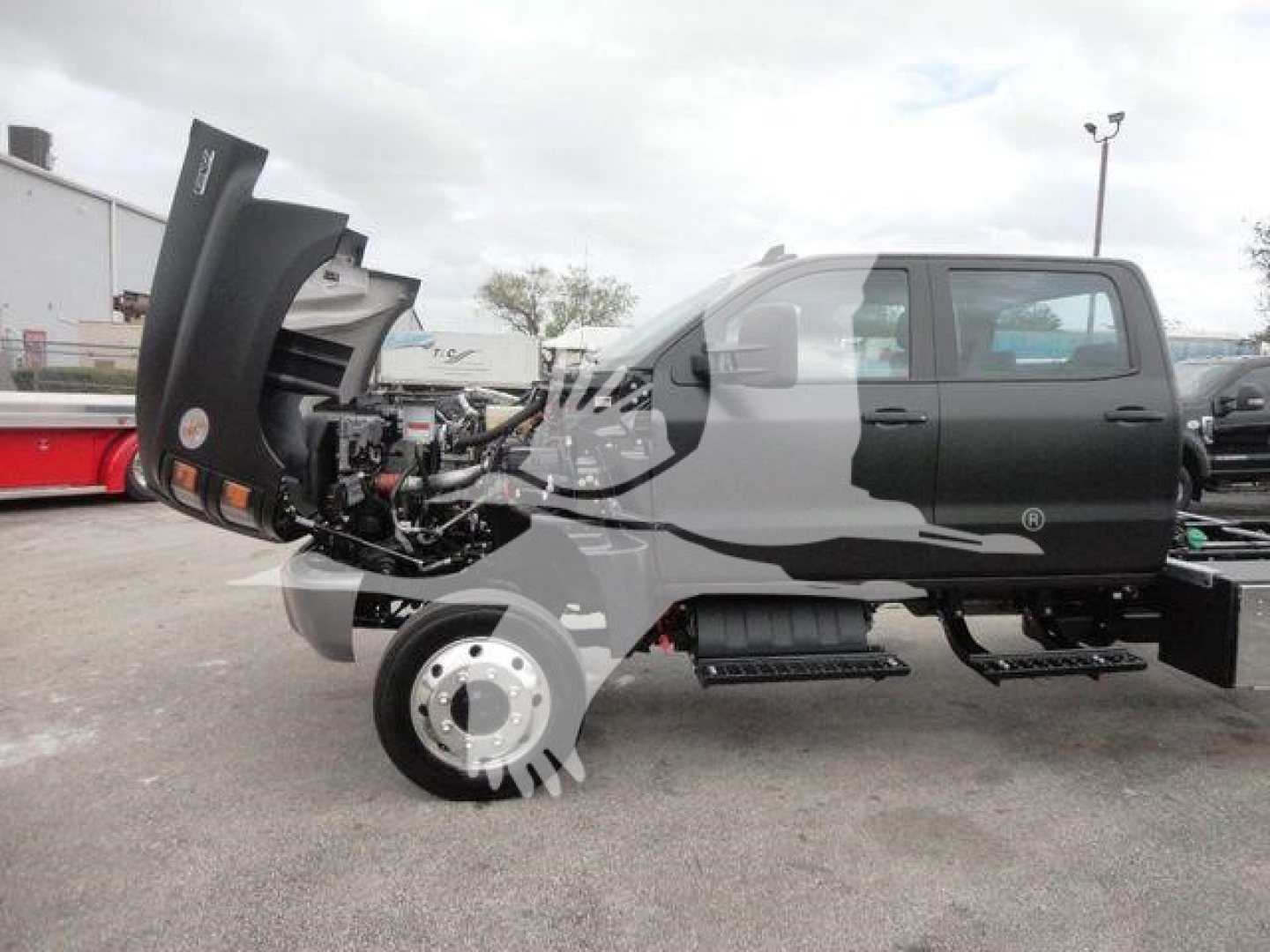 Truck cab and engine bay with hood open showing front axle and wheel in a rollback truck configuration.