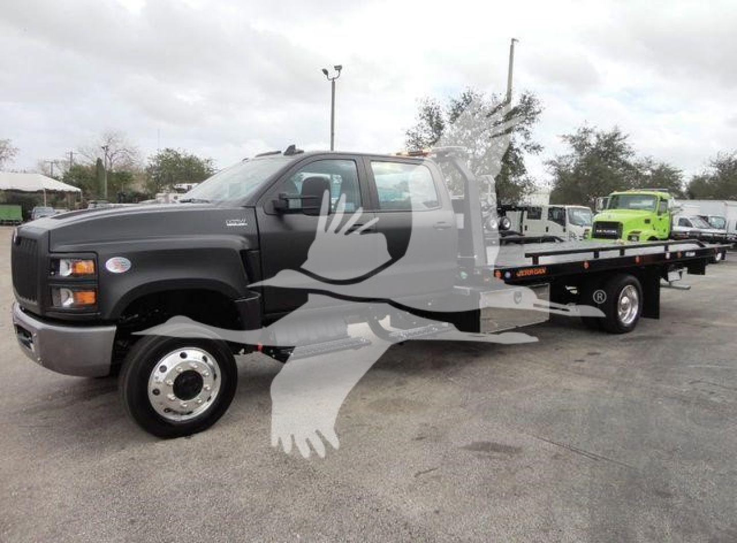 Truck cab and long flatbed rollback tow truck in a dealership lot showing International badge and extended wheelbase.