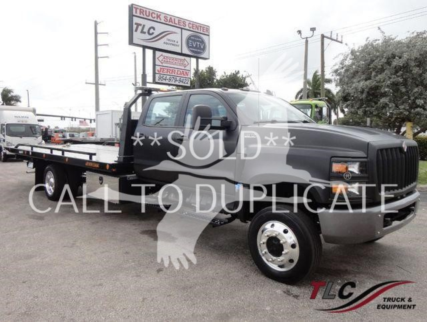 Flatbed tow truck on lot with 'SOLD' overlay and TLC logo in corner. Visible text includes 'TRUCK SALES CENTER' sign in background and 'TLC TRUCK & EQUIPMENT' watermark. Other legible words: 'SOLD' across center, 'CALL TO DUPLICATE' overlai