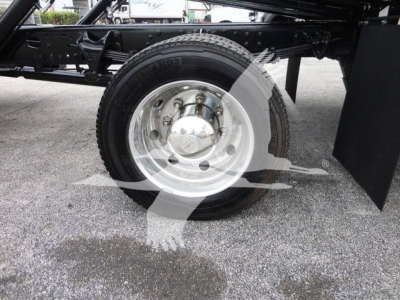 Truck wheel and suspension detail showing front axle with chrome hubcap and tire on a new 2023 International CV rollback truck.