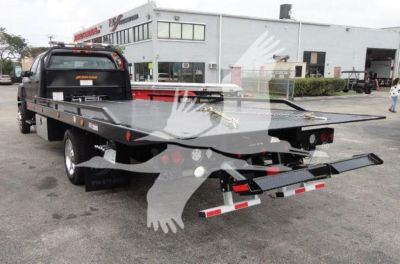 Flatbed rollback tow truck with steel deck and rear ramps visible in parking lot.