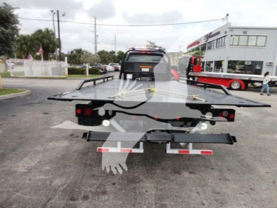 Tractor-trailer tow truck with a flatbed in a dealership lot; back view showing platform and taillights.