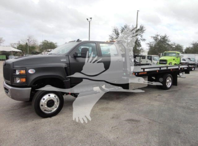 Truck cab and long flatbed rollback tow truck in a dealership lot showing International badge and extended wheelbase.